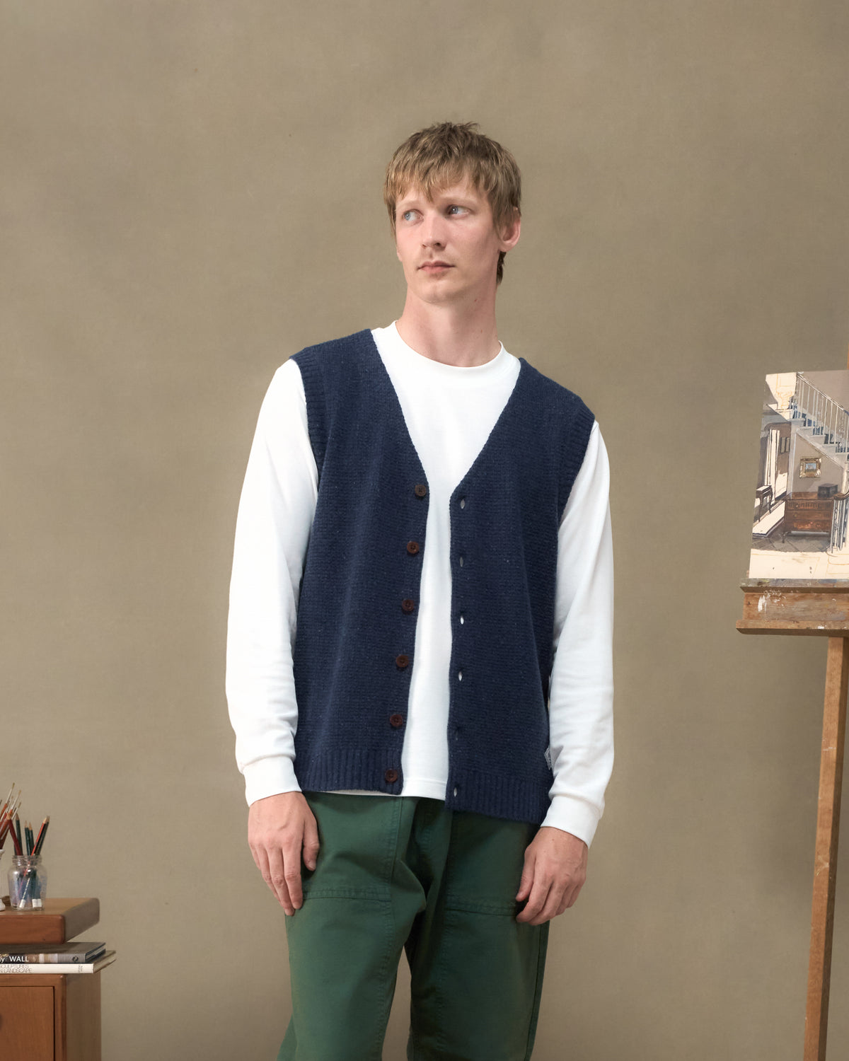 Model wearing the Fera Curlew Merino Vest in Navy over a white long sleeve in an artist's studio