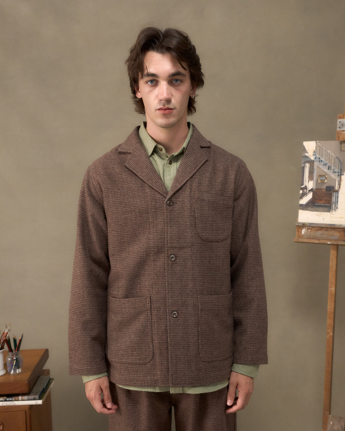 Model wearing the Fera Studio Jacket in Tweed over a green shirt, front view beside a painter's easel
