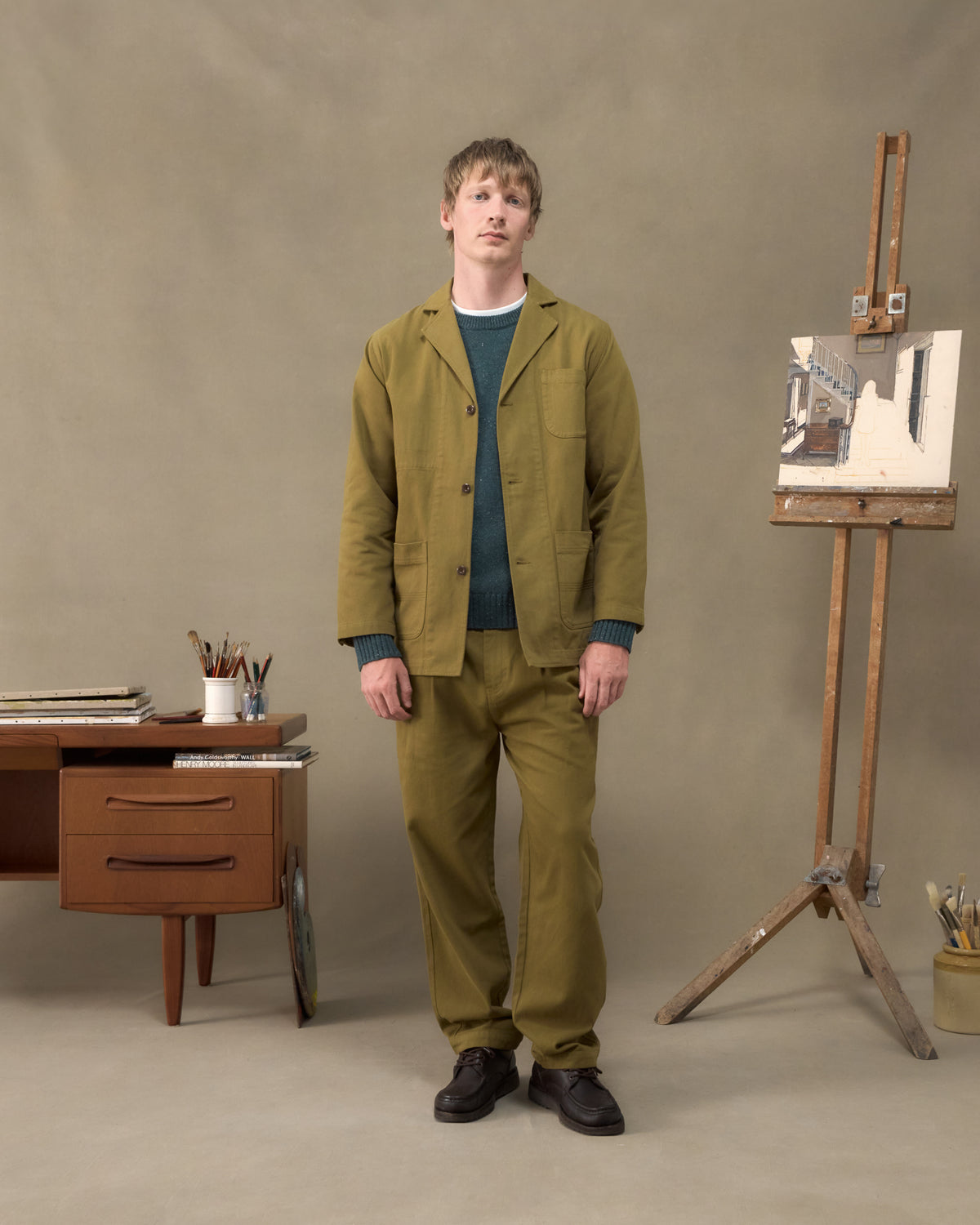 Model wearing the Fera Studio Jacket and Uniform Trousers in Moss over a teal Peewit Knit