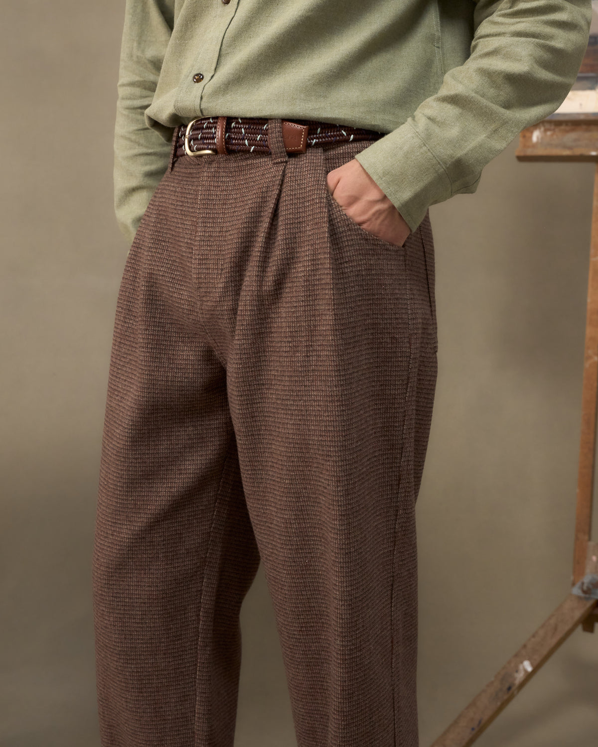 Fera Uniform Trousers in Tweed worn with a leather belt and green shirt, hand in the side pocket