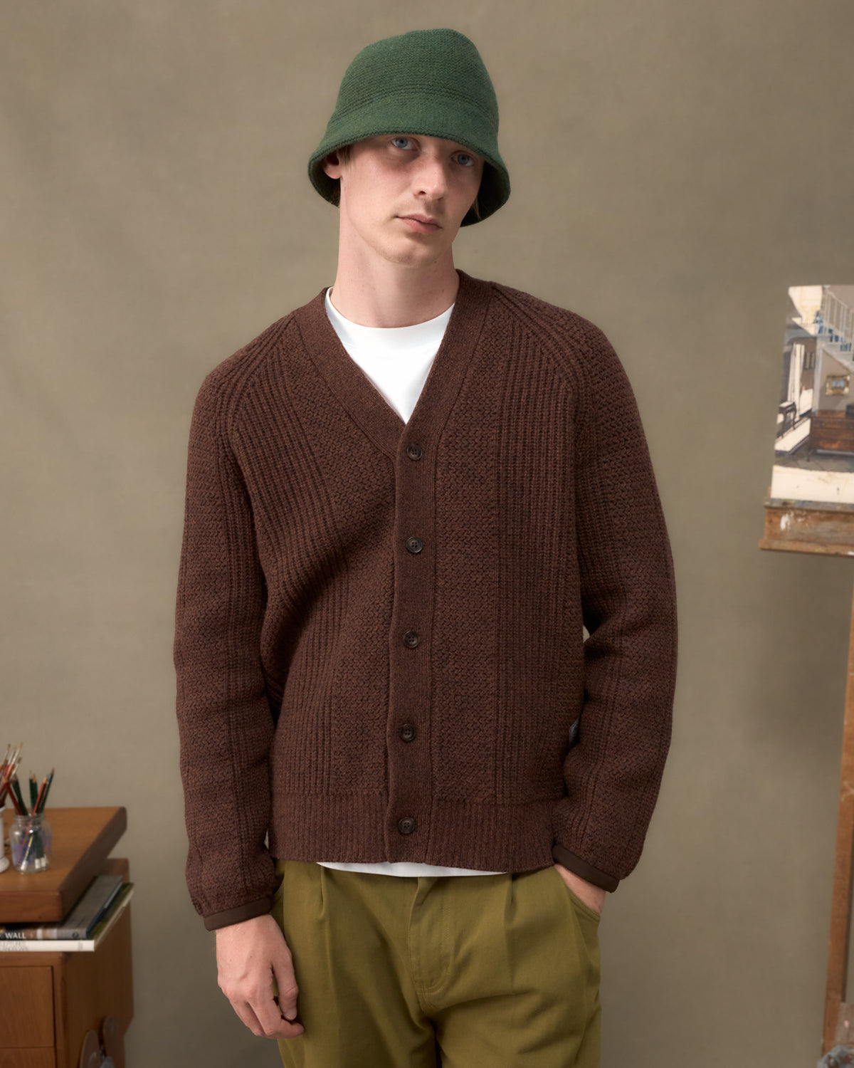 Model wearing the Fera Brigade Cardigan in Brown Marl with a green bucket hat, front view