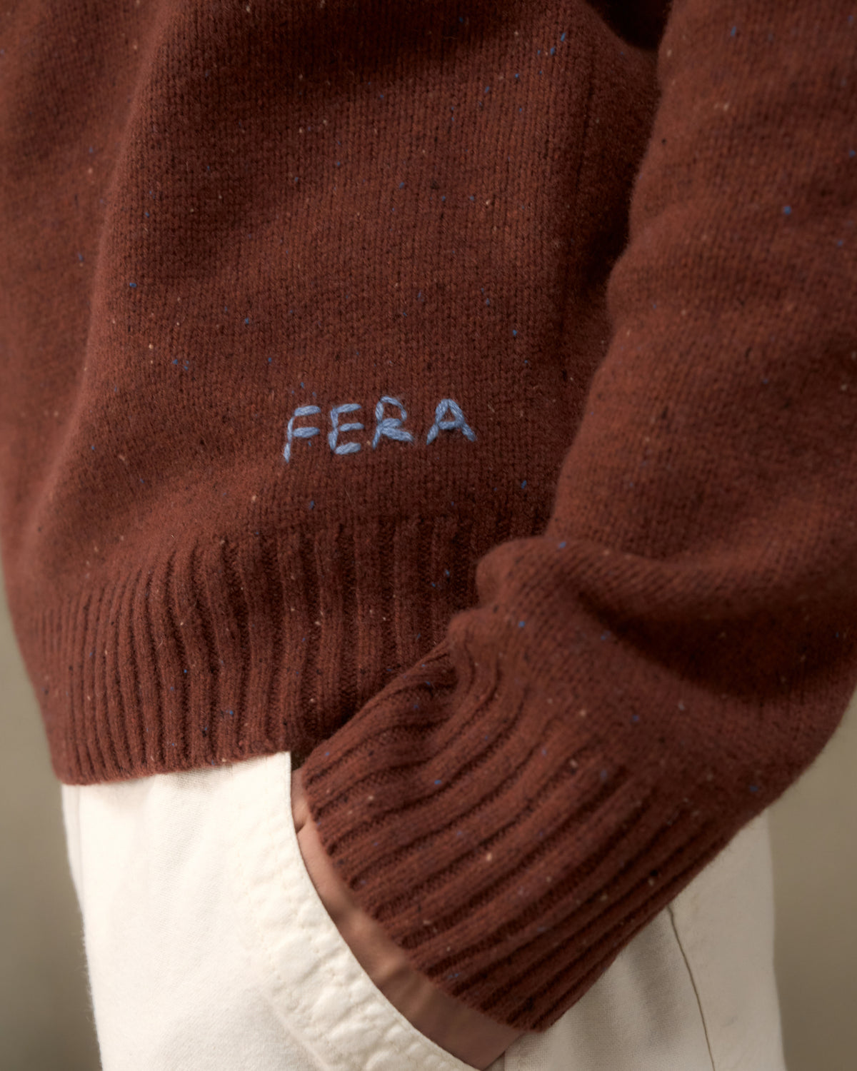 Close-up of the Fera Peewit Knit in Copper showing the hand-embroidered Fera logo above the ribbed hem