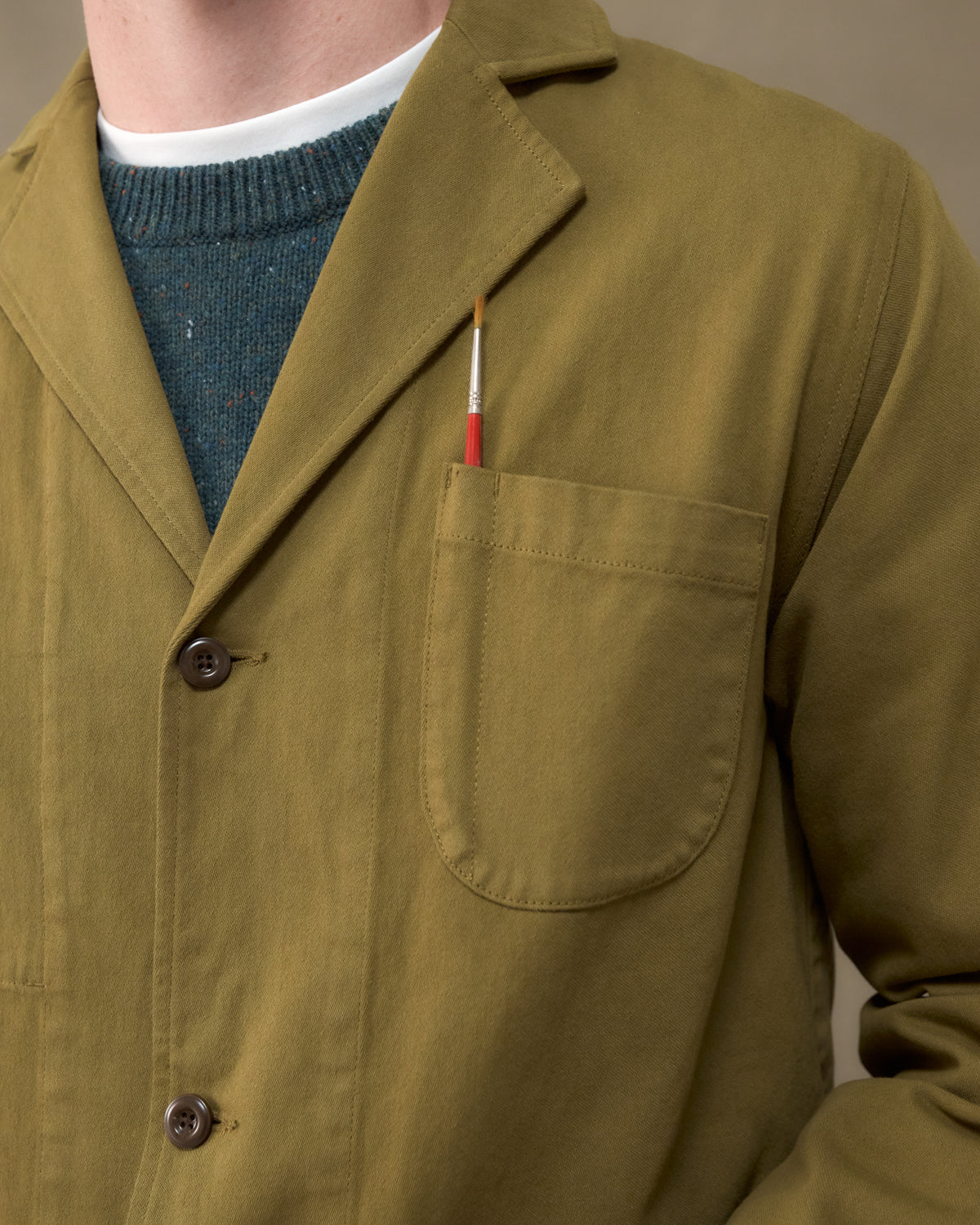 Close-up of the Fera Studio Jacket in Moss showing the chest pocket with a paintbrush and corozo buttons
