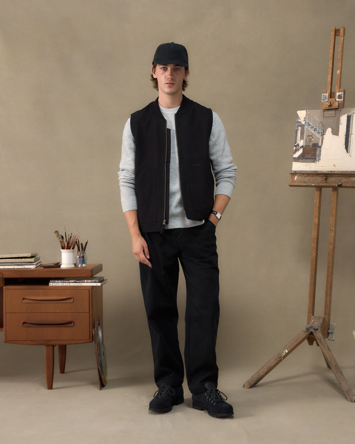 Model wearing the Fera Poacher Gilet in Black over a grey waffle top in an artist's studio