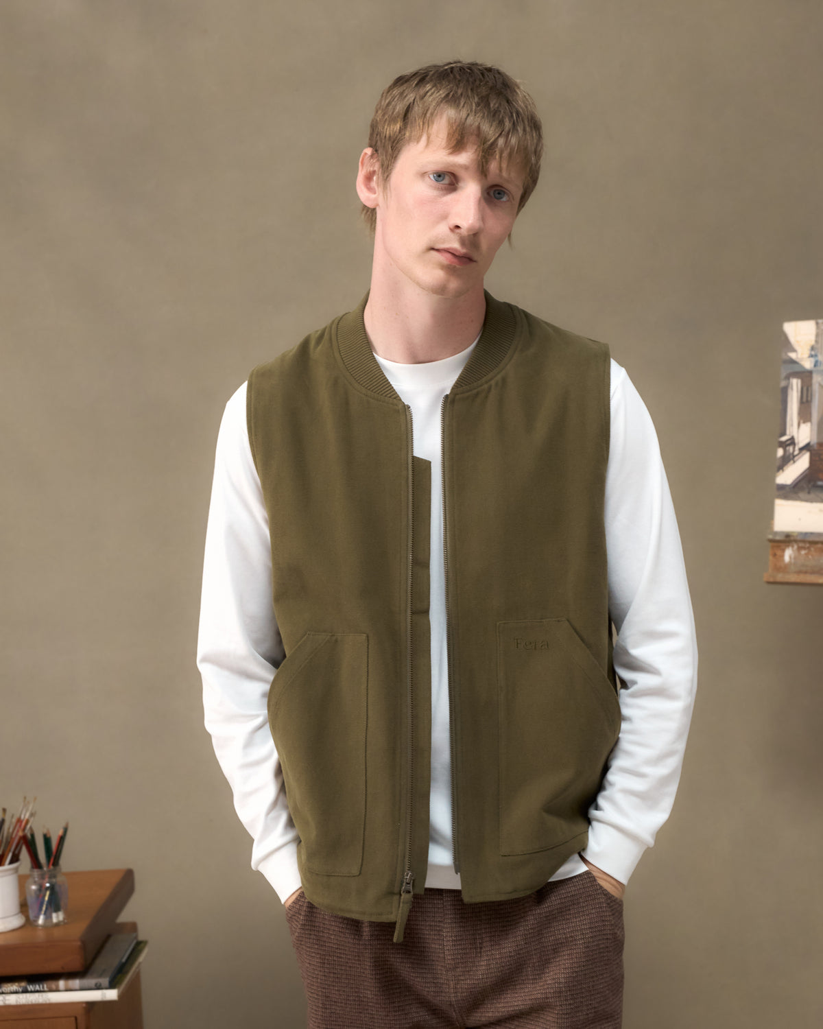 Model wearing the Fera Poacher Gilet in Marsh Green over a white long sleeve in an artist's studio