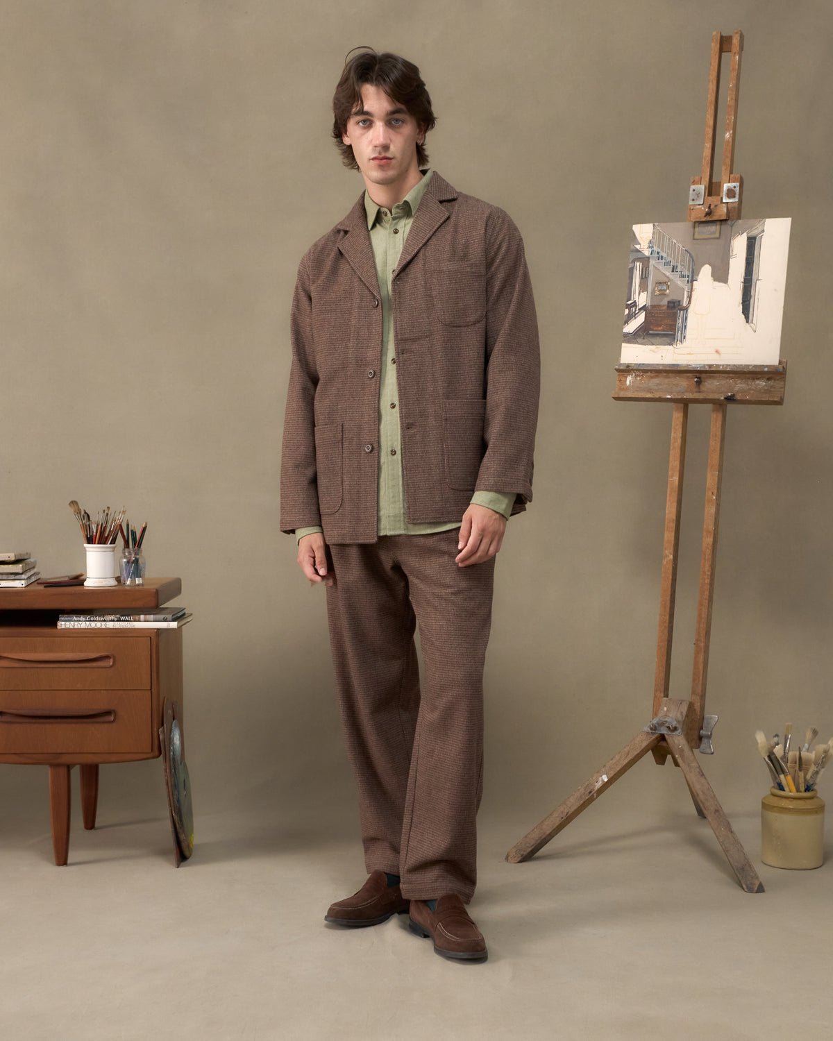 Model wearing the Fera Studio Jacket and Uniform Trousers in Tweed with a green Avon Shirt in an artist's studio