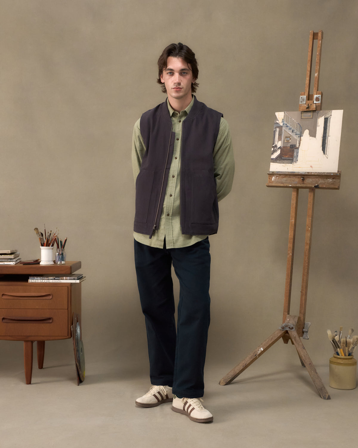 Model wearing the Fera Poacher Gilet in Washed Blue, front view beside a painter's easel