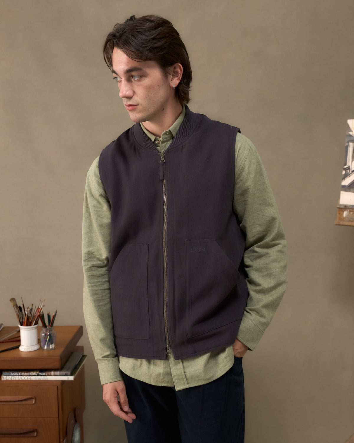 Model wearing the Fera Poacher Gilet in Washed Blue over a green Fera Avon Shirt in an artist's studio
