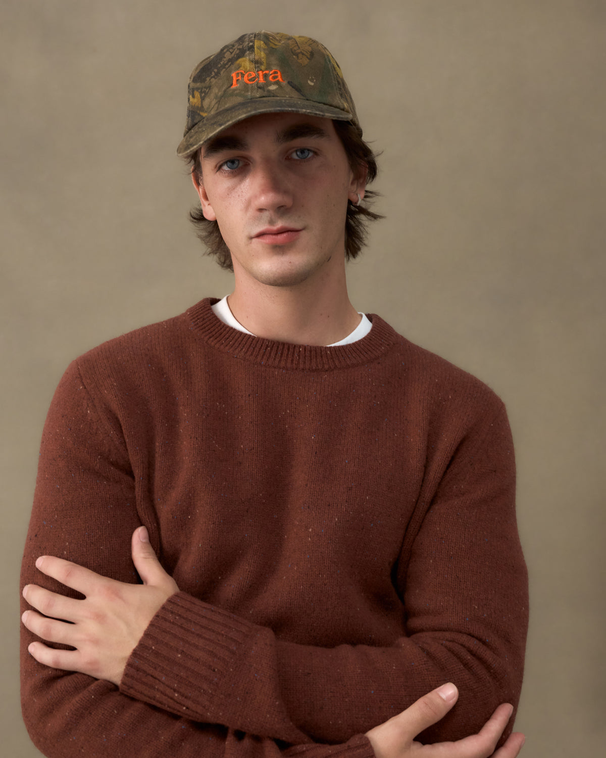 Portrait of a model wearing the Fera Peewit Knit in Copper Merino lambswool with a camouflage Fera cap