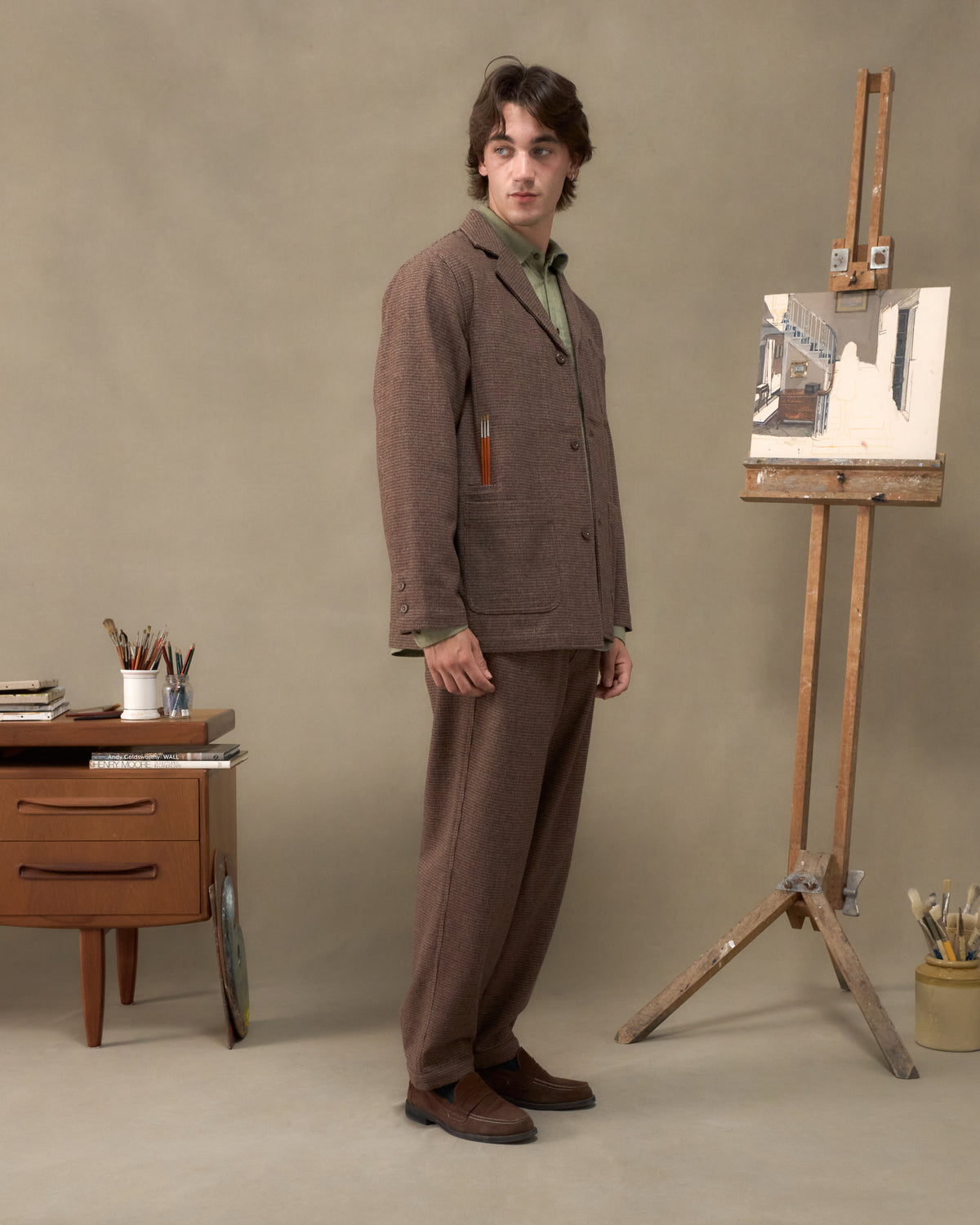 Model wearing the Fera Studio Jacket and Uniform Trousers in Tweed, side view with brushes in the chest pocket